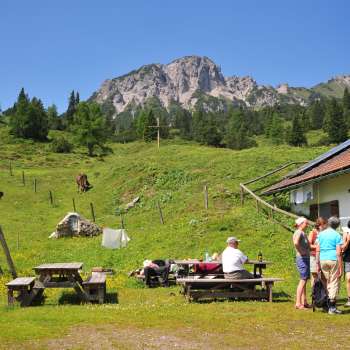 Blick auf die Berge von der Alpe Guschg an der mehrere Personen Pause machen und genießen
