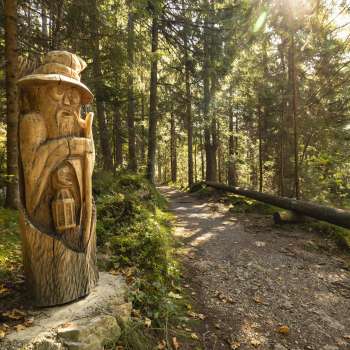 Holzfigur mit Laterne am WalserSagenWeg im mystischen Waldlicht