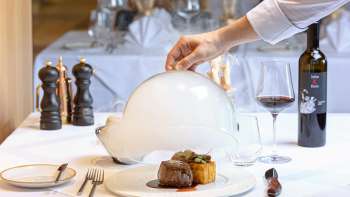 Serviertes Gourmetgericht mit Fleisch und Beilage, dekorativ unter einer weissen Cloche im edlen Restaurant Alpspitz angerichtet.