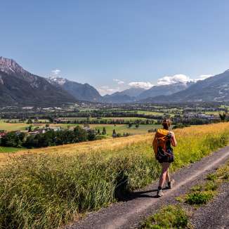 Frau wandert auf einem Feldweg mit Panorama-Aussicht über das Rheintal in Liechtenstein