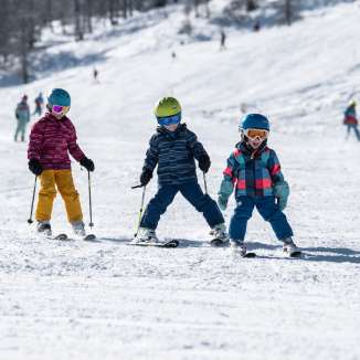 Drei Kinder lernen Skifahren im Familienskigebiet Malbun in Liechtenstein bei Sonnenschein und Pulverschnee