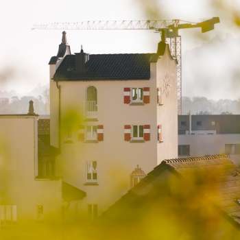 Nahaufnahme des historischen Turms des Rathauses Vaduz mit markanten roten Fensterläden, umgeben von Baustellenkränen im Hintergrund.