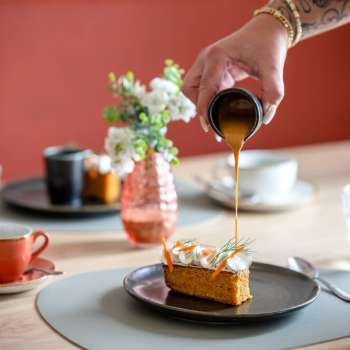 Dessert wird mit Karamellsauce übergossen, im Hintergrund Kaffeetassen und stilvolle Tischdeko