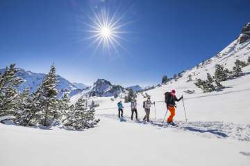 Gruppe beim Schneeschuhwandern durch die verschneite Landschaft am Schönberg bei Malbun unter strahlender Wintersonne.
