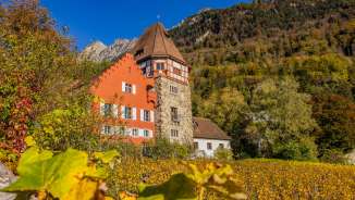 Das Rote Haus in Vaduz, Liechtenstein, eingebettet in bunte Herbstlandschaft und Weinberge am Fusse der Berge.