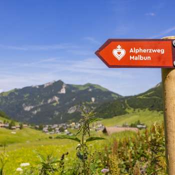 Wegweiser Alpherzweg mit Bergdorf Malbun im Hintergrund