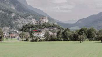 Majestätische Aussicht auf Burg Gutenberg in Balzers, umgeben von grünen Feldern und den beeindruckenden Alpen.