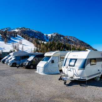 Wohnmobile und Wohnwagen stehen auf einem verschneiten Stellplatz in Malbun mit Blick auf die Alpen