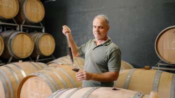 Harry Zech entnimmt Wein zur Verkostung mit einer Pipette aus dem Barriquefass – traditionelle Weinherstellung in Schaan.