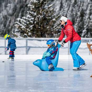 Familie auf dem Eisplatz beim Schlucher-Treff in Malbun, unterstützt von einer Eislaufhilfe in Form eines blauen Tieres