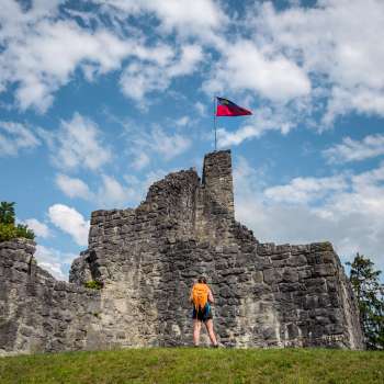 Wanderin steht vor den imposanten Ruinen der Burg Schellenberg unter blauem Himmel mit Flagge.