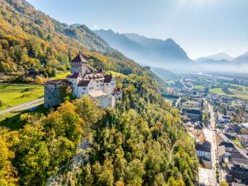 Blick auf Schloss Vaduz in Liechtenstein mit herbstlichen Farben, Bergen und dem Rheintal im Hintergrund
