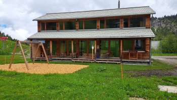 Aussenaufnahme des Malbipark-Bistro mit einem Spielplatz und Wiese im Vordergrund