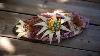 Ein kunstvoll angerichteter Holzbrett mit verschiedenen Wurstsorten, Käse und Dekoration aus essbaren Blumen, serviert auf einem Holztisch.