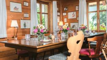 Einladender Gastraum mit Holzdecke, liebevoll dekoriertem Tisch und hellem Fensterblick