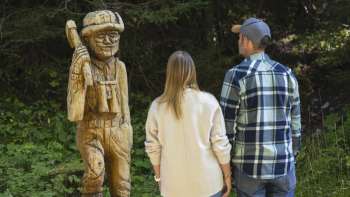Spaziergänger betrachten geschnitzte Holzfiguren entlang des WalserSagenWegs Spaziergänger betrachten geschnitzte Holzfiguren entlang des WalserSagenWegs