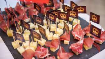 Fingerfood Appetithäppchen mit Käsewürfeln und luftgetrocknetem Schinken, dekoriert mit individuell bedruckten Markenfähnchen auf einer Schieferplatte