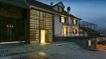 Modern beleuchtetes Kulturhaus Rössle in Mauren bei Abenddämmerung, mit Glasfassade, historischem Gebäudeanbau und gepflastertem Vorplatz.