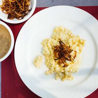 Traditionelle Käsknöpfle mit Röstzwiebeln und Apfelmus aus Liechtenstein auf weißem Teller