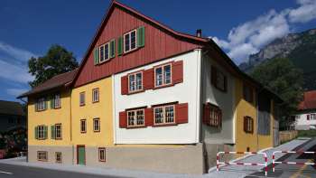Traditionelles Landweibels-Huus in gelb-roter Fassadengestaltung vor Bergkulisse in Liechtenstein.