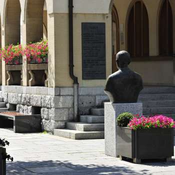 Blick auf den Eingangsbereich des Rathauses Vaduz mit Blumenarrangements, historischer Büste und breiten Steinstufen – ein kulturelles Wahrzeichen im Zentrum von Vaduz.