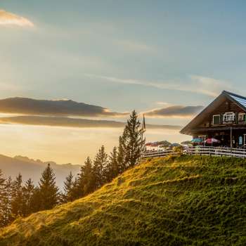 Gadafurahütte auf sonnenbeschienener Bergwiese mit Blick auf die Berge und Sonnenuntergang