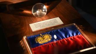 Ausstellungsstück in der Schatzkammer Liechtenstein: Liechtensteiner Flagge mit goldener Krone und gläserne Kugel mit historischem Fundstück