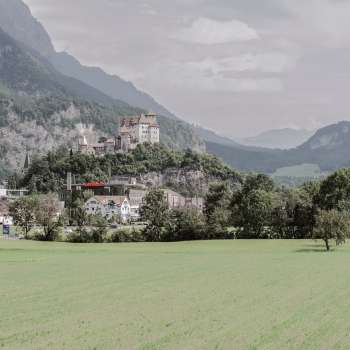 Majestätische Aussicht auf Burg Gutenberg in Balzers, umgeben von grünen Feldern und den beeindruckenden Alpen.