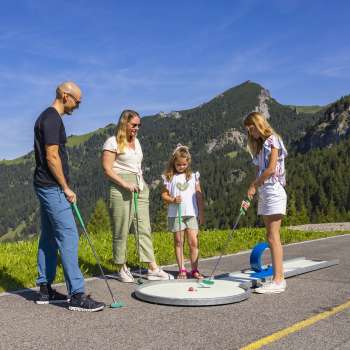  Familie spielt gemeinsam Minigolf in den Bergen von Malbun bei strahlendem Sonnenschein