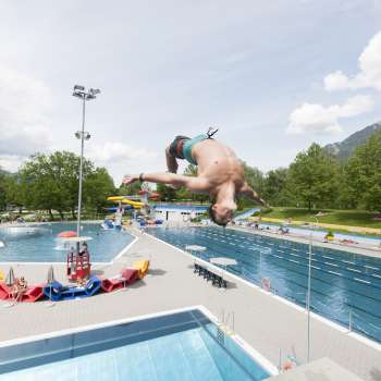 unge springt mit Salto vom 1-Meter-Brett ins Becken des Schwimmbads Mühleholz – Sommerfreude pur.