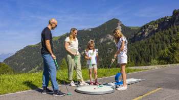  Familie spielt gemeinsam Minigolf in den Bergen von Malbun bei strahlendem Sonnenschein
