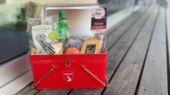 Eine rote Box gefüllt mit Snacks wie Riebelmais, Käse, einem Apfel und weiteren Leckereien