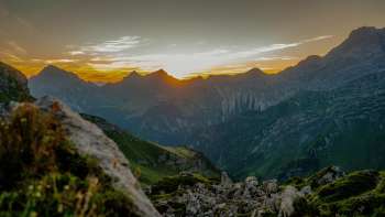 Sonnenuntergang am Grat – Die Sonne versinkt hinter den Bergspitzen und taucht das alpine Panorama in warme Abendfarben