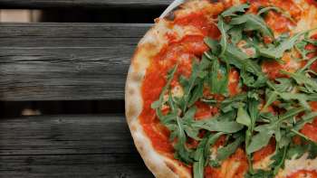 Frische Pizza mit Tomatensauce und Rucola, serviert auf rustikalem Holztisch Frische Pizza mit Tomatensauce und Rucola, serviert auf rustikalem Holztisch