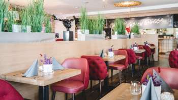 : Großzügig gedeckte Tische im PUR Restaurant & Bar mit roten Stühlen und floraler Tischdekoration.