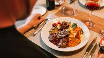 Detailaufnahme eines Hauptgerichts mit Fleisch, Gemüse und feinen Saucen, begleitet von Rotwein