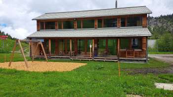 Aussenaufnahme des Malbipark-Bistro mit einem Spielplatz und Wiese im Vordergrund