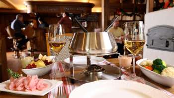 Nahaufnahme von Käsefondue-Set mit frischem Brot, Gemüse und Wein im stilvollen Ambiente