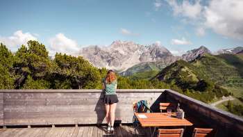 Eine Frau geniesst die Aussicht von der Aussichtsterrasse Sareis auf die Liechtensteiner Alpen und das Rheintal bei klarem Wetter