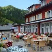Sonnige Terrasse des Restaurants mit gedeckten Tischen, Sonnenschirmen und Alpenblick.