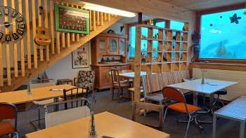 Gastraum mit Fensterfront und Dekoration – Tische und Stühle in einem offenen Raum mit großen Fenstern und Blick auf die grüne Außenanlage.