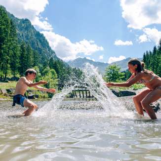 Kinder planschen im Gänglesee bei Steg, umgeben von Wäldern und Bergen – Naturerlebnis und Abkühlung in Liechtenstein