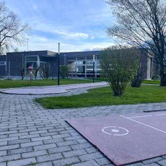Minigolfanlage mit mehreren Bahnen auf einer gepflegten Grünfläche zwischen Schaan und Vaduz, im Hintergrund modernes Gebäude und Bäume.