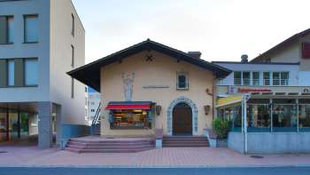 Außenansicht des Alten Kino Vaduz mit Schriftzug über dem Eingang und roten Markisen, zwischen zwei modernen Gebäuden gelegen.