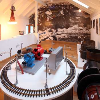 Modell einer Turbine auf einer Ausstellungsplattform im Lawena Museum, im Hintergrund historische Schwarzweißaufnahmen.