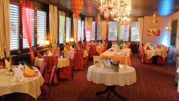 Festlich dekorierter Gastraum mit runden Tischen, bunter Tischdeko und Kronleuchtern