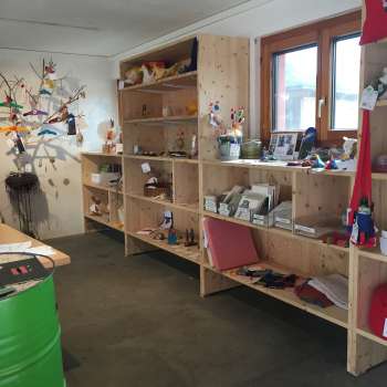Innenraum des Birkahoflädile mit Holzregalen voller regionaler Produkte, dekorativ gestaltet mit bunten Elementen – Hofladen in Liechtenstein.