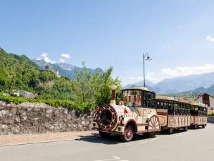 Citytrain fährt durch Vaduz, im Hintergrund Schloss Vaduz und die Alpen bei strahlendem Sonnenschein
