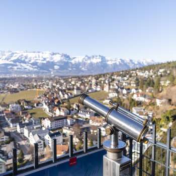 Fernrohr am Schlossweg-Aussichtspunkt Känzile mit Blick auf Vaduz und das verschneite Alpenpanorama im Hintergrund.