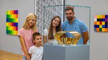 Familie mit zwei Kindern betrachtet eine gläserne Vitrine mit goldener Skulptur im Museum